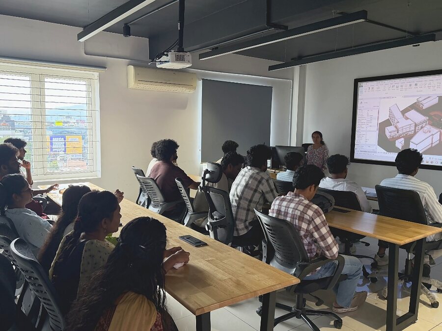 Learners at desks in a Bumblebee Inc classroom while the trainer presents a Revit building model on the screen